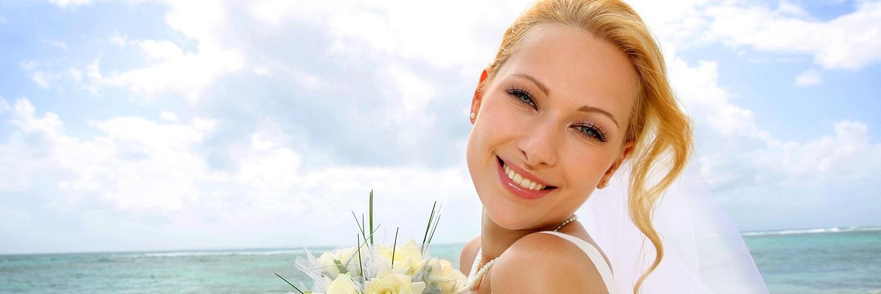 woman in wedding veil smiling with ocean behind her